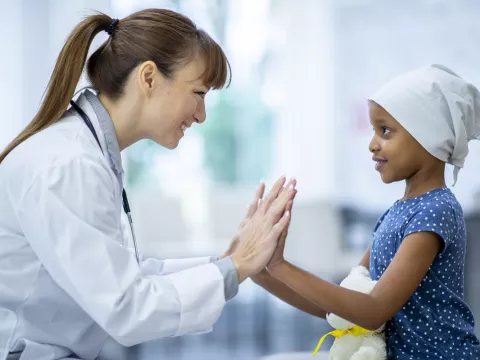 Encouraging doctor with young cancer patient, they are clapping hands together.