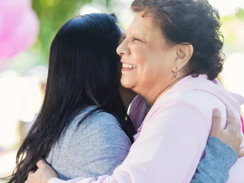 Two women hug at a breast cancer walk.